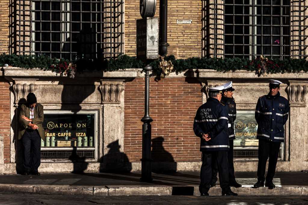 Morador de rua fuma próximo a policiais municipais em serviço na Piazza Venezia, no centro de Roma, em 1º de janeiro de 2019. (Foto: Laurent EMMANUEL / AFP)