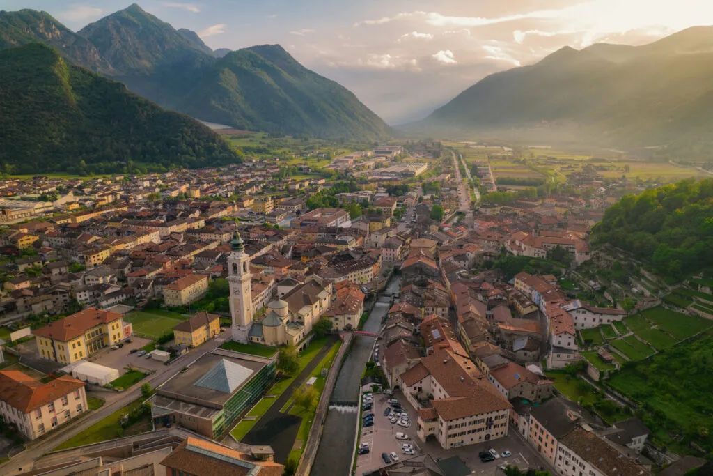 Vista aérea da Valsugana, região do Trentino, cercada por montanhas e rica em história e cultura.