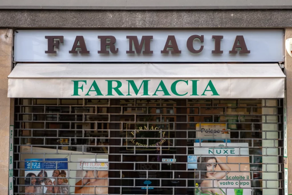 Fachada de uma farmácia italiana com grades fechadas, prática comum fora do horário comercial