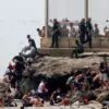 Migrantes cruzam a nado a fronteira do Marrocos junto ao quebra-mar de El Tarajal, em Ceuta, exclave da Espanha no norte da África, nesta quinta-feira (30), sob observação de agentes da Guarda Civil espanhola. (Foto: AFP)