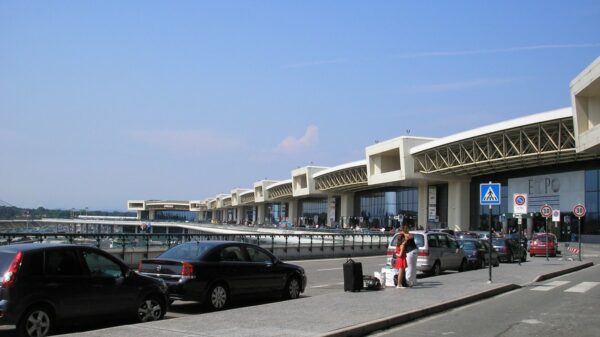 Fachada do Aeroporto de Malpensa, em Milão, com carros e passageiros em frente ao terminal.
