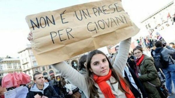 Un giovane regge un cartello con la scritta "Non è un paese per giovani" durante una protesta di piazza in Italia, simbolo del malcontento che spinge la nuova generazione a emigrare all'estero.