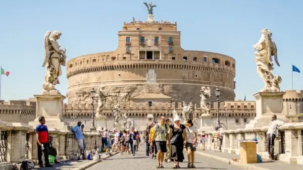 Turistas caminham pela Ponte Sant’Angelo, em Roma, com o Castel Sant’Angelo ao fundo. Também conhecido como Mausoléu de Adriano, o monumento foi posteriormente utilizado como fortaleza e castelo pelos papas. Foto: Depositphotos