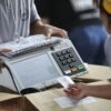 Funcionários da Justiça Eleitoral manuseiam uma urna eletrônica durante os preparativos para a votação no Brasil | Foto: Reprodução