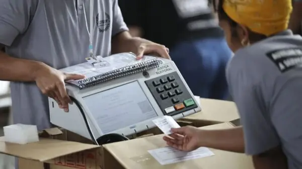 Funcionários da Justiça Eleitoral manuseiam uma urna eletrônica durante os preparativos para a votação no Brasil | Foto: Reprodução
