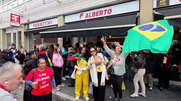 Eleitores brasileiros com bandeiras do Brasil e camisetas de apoio aos candidatos se reúnem nas proximidades do local de votação em Milão, durante o segundo turno das eleições presidenciais, neste domingo (25)
